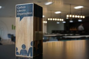 Wooden Carbon Literate Organisation award standing on a table in a modern, softly lit meeting room.